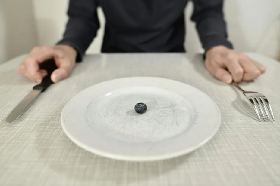 A person with a tiny portion of food on a big plate.