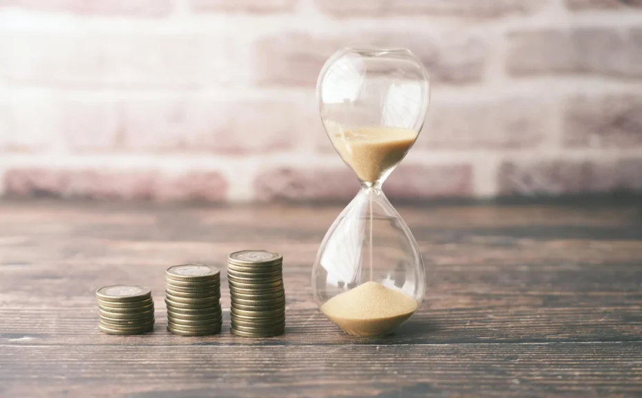 An hourglass and coins depicting time and money.